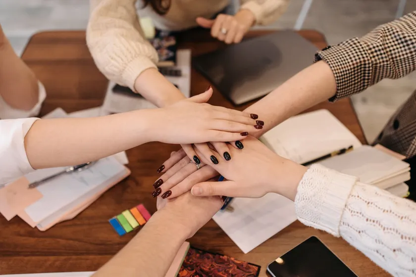 Manos de un equipo uniéndose sobre una mesa de trabajo, en gesto de colaboración
