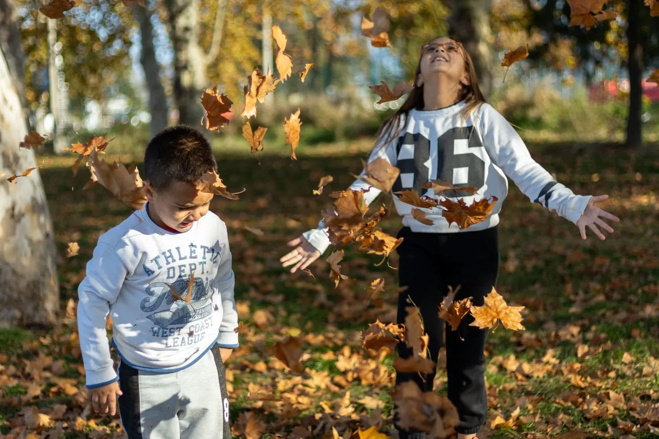 Niños jugando con hojas de otoño en un parque soleado